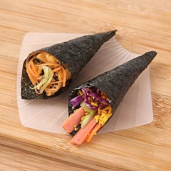 Two cone-shaped sushi wraps filled with vegetables and rice, placed on a translucent square plate over a wooden surface.