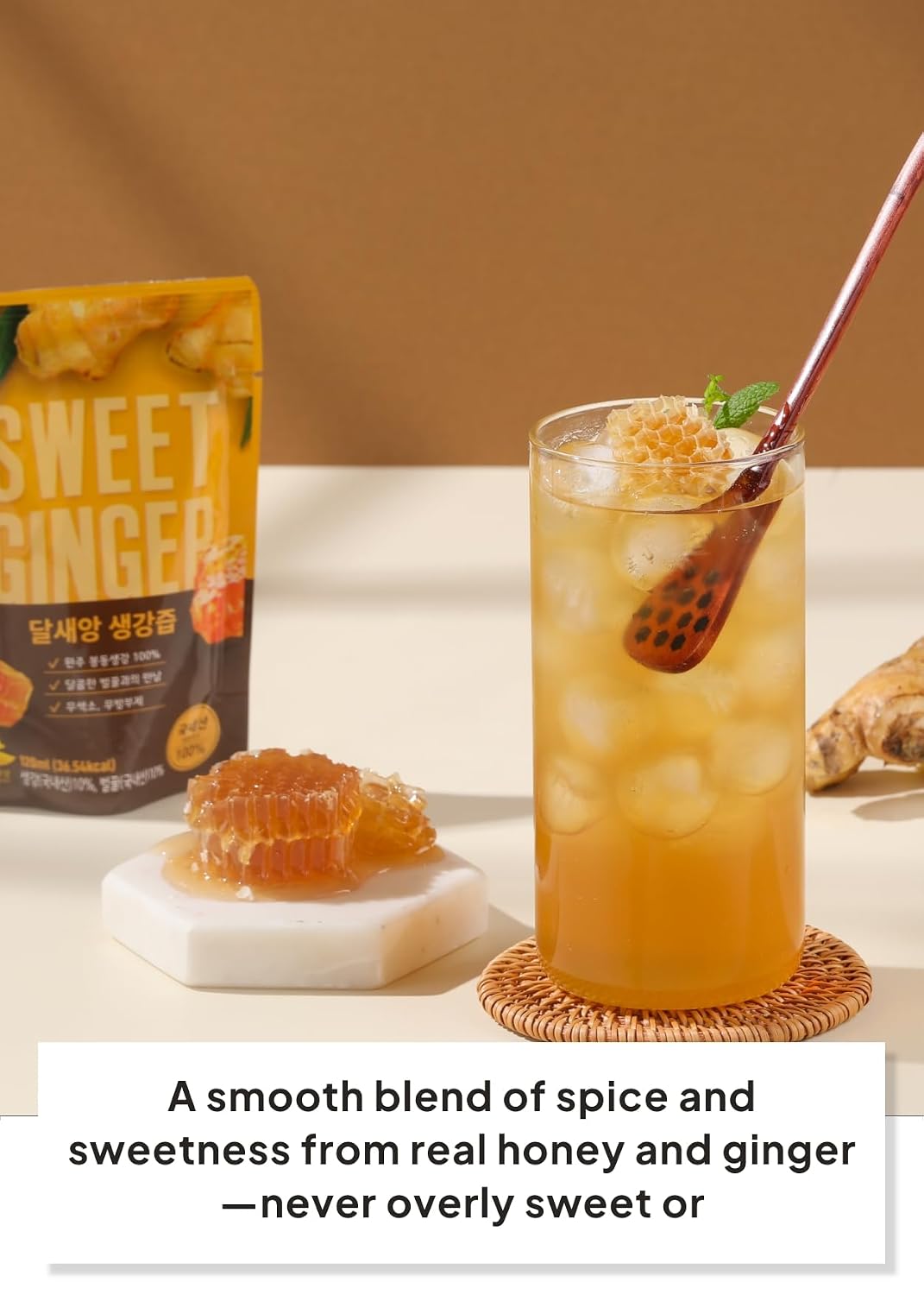 A glass of iced ginger drink with ice and a honeycomb piece on a coaster, next to a small dish of honey and a stand-up pouch labeled Dalsaeang Sweet Ginger, with a text banner at the bottom.